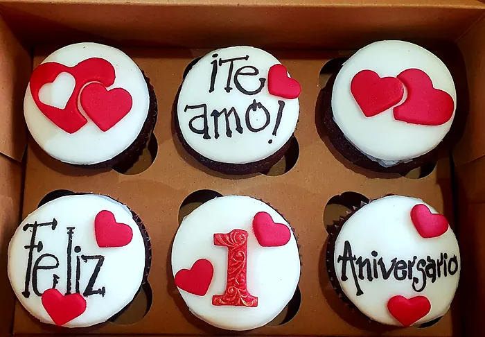 Seis cupcakes con fondant blanco y corazones rojos que dicen Te amo, Feliz 1 Aniversario