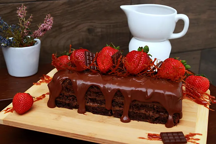 Pastel de chocolate en capas bañado en chocolate, con fresas, trozos de chocolate e hilos de caramelo