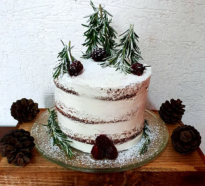 Pastel semidesnudo con árboles de romero, moras y azúcar glass como nieve, rodeado de piñas