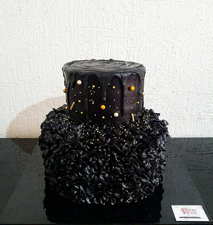 Pastel negro de dos pisos con escurrido de chocolate, volantes y perlas doradas